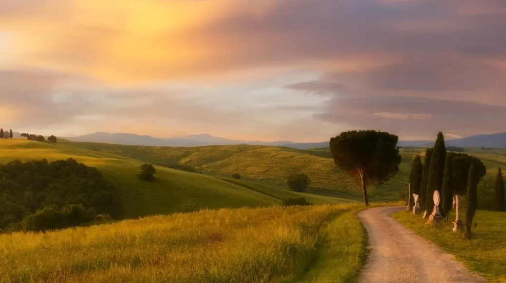 Campagna al tramonto con colline e una strada sterrata tra i cipressi